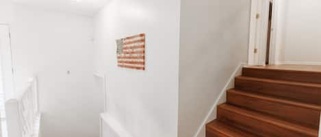Eine Treppe mit Holzbodenstufen führt zu einer Zwischenebene, an den Wänden sind weiße Wände und eine kleine amerikanische Flagge zu sehen.