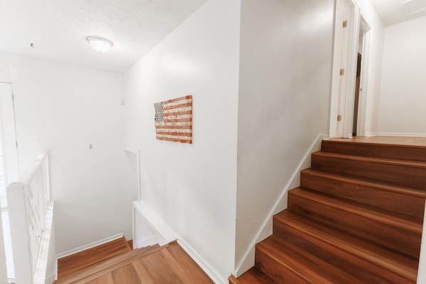 Eine Treppe mit Holzbodenstufen führt zu einer Zwischenebene, an den Wänden sind weiße Wände und eine kleine amerikanische Flagge zu sehen.