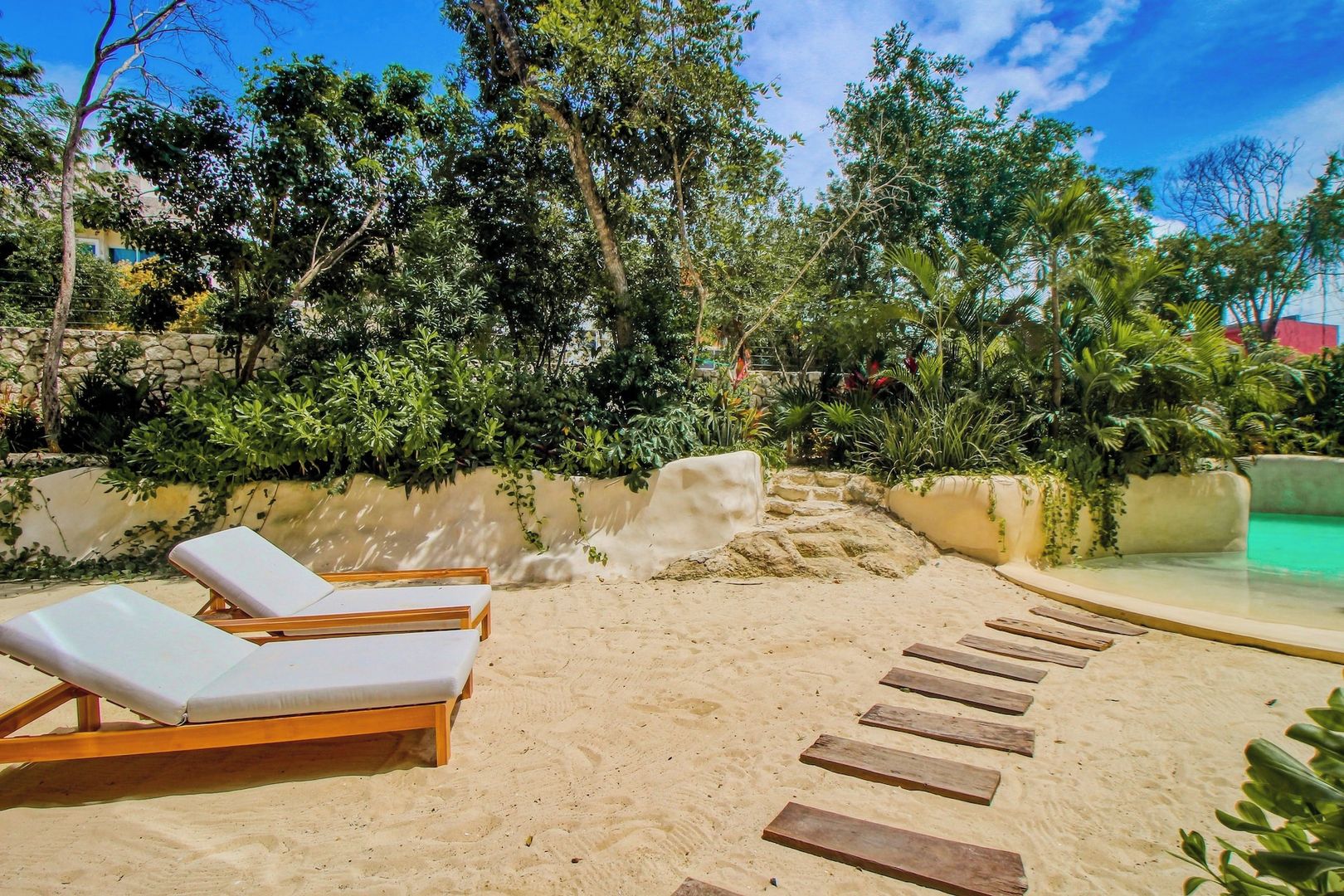 A sandy beach area with lounge chairs and a pool.