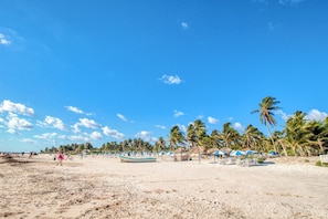 A beach with palm trees, beach umbrellas, and a few people. - Embrace the ultimate Tulum experience in our exclusive loft, perfectly... (Tulum)