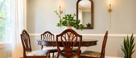 A dining room with a round table, four wooden chairs, a potted plant, and wall-mounted sconces.