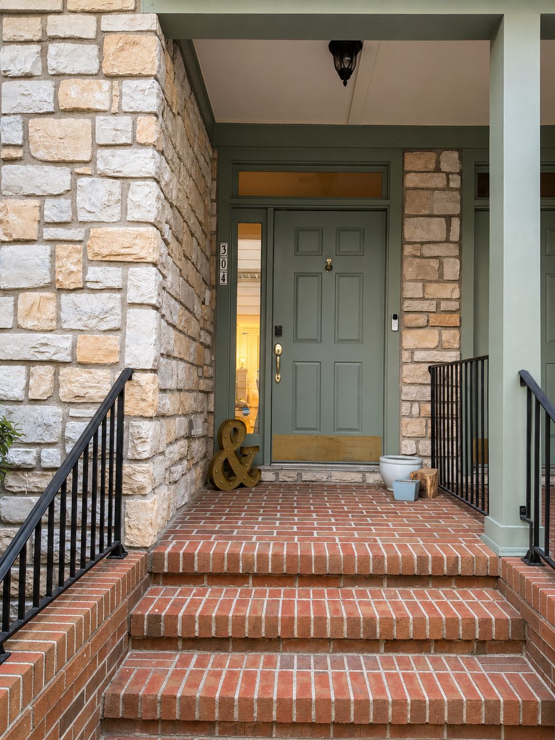 A stone facade with a green door, a brick entrance, and a black metal railing.