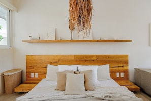 A bedroom with a wooden headboard, a bed with white bedding, a bedside table, a wicker basket, and a hanging decor piece. - Please note: electricity is not included in reservations longer than 28... (Tulum)