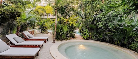 Ein Poolbereich mit Liegestühlen und üppiger tropischer Vegetation.
