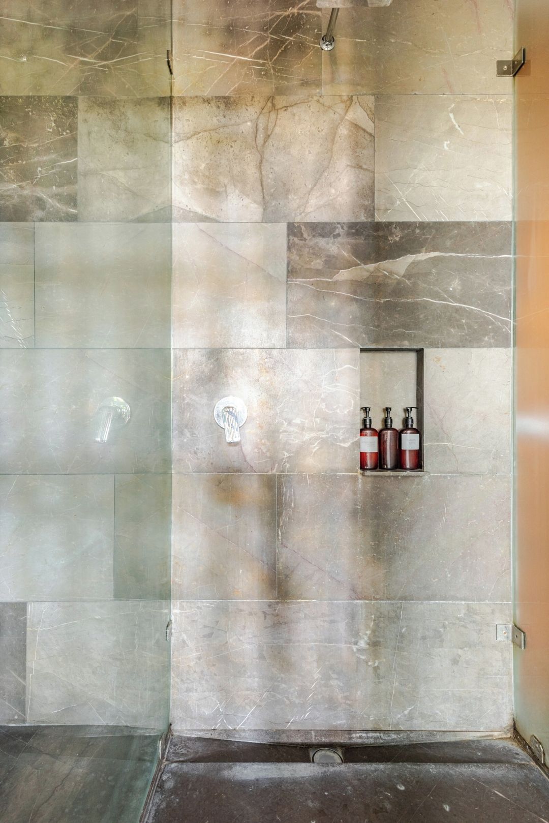 Une salle de bain avec un mur en marbre, une douche et une étagère contenant des articles de toilette.