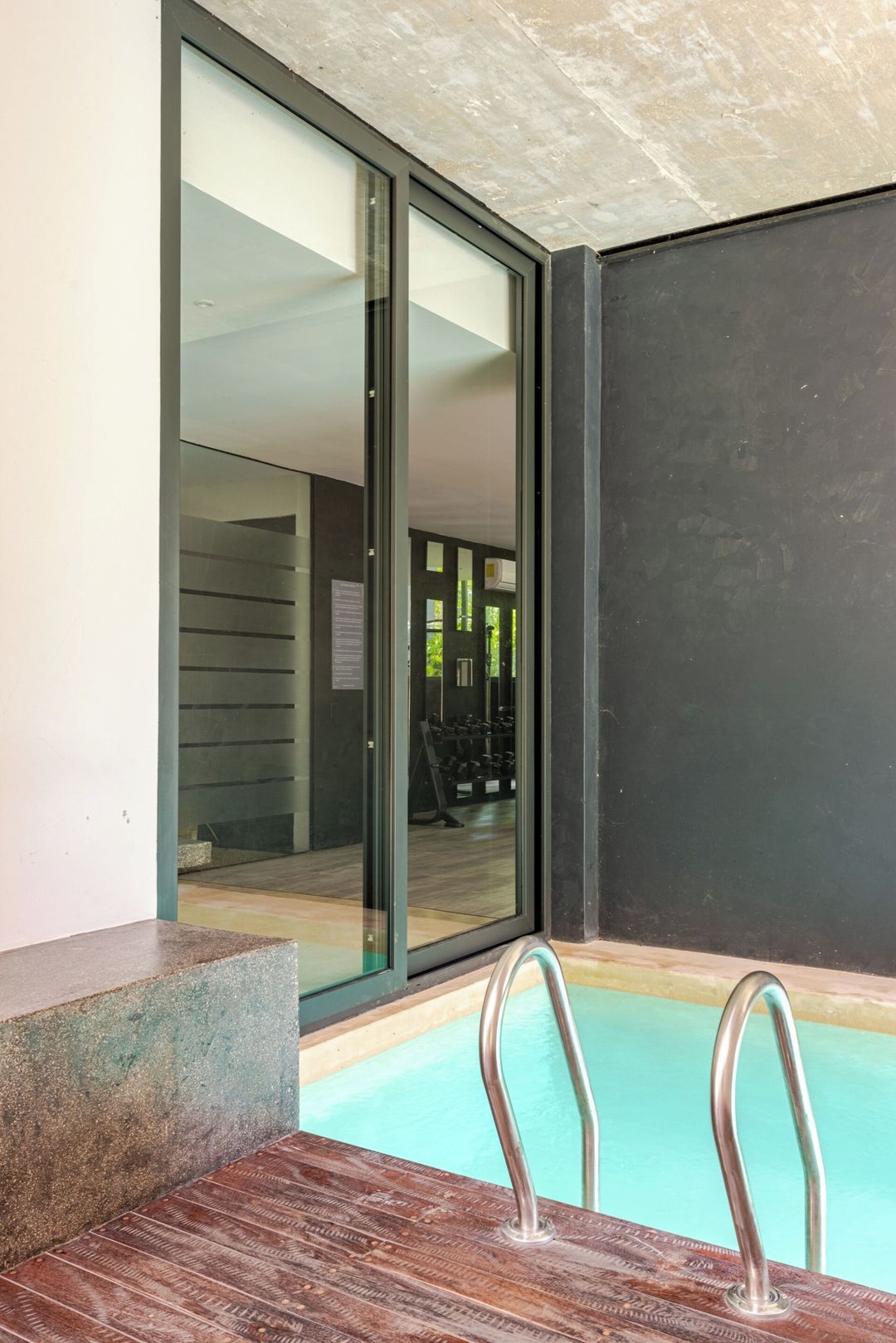 A swimming pool with metal railings, a glass door leading to an indoor area, and a concrete structure.