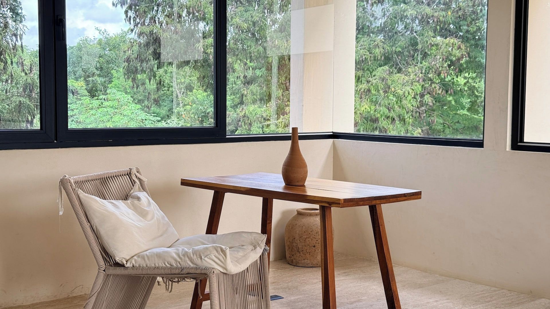 A room with a woven chair, a wooden table, and a vase.