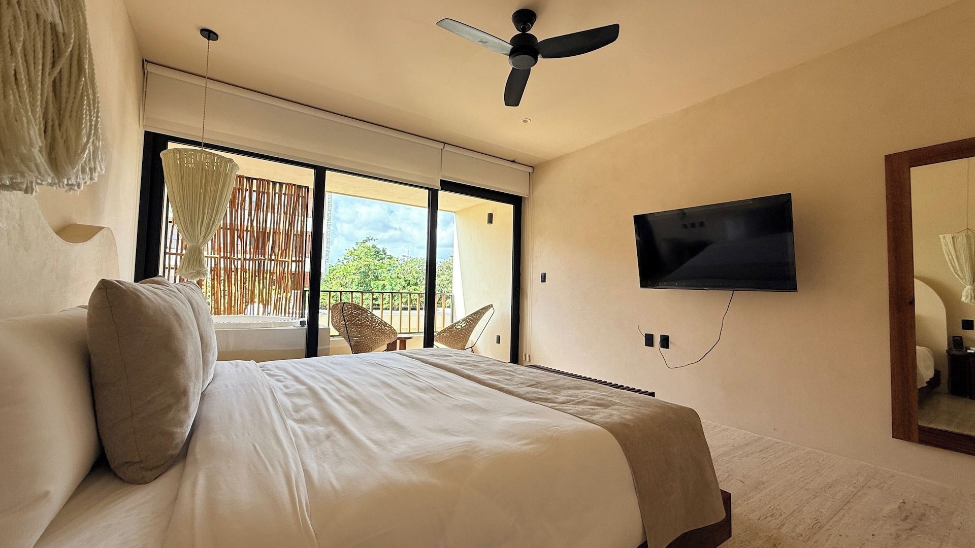 A bedroom with a bed, a television mounted on the wall, and a view of the outdoors through a sliding door.