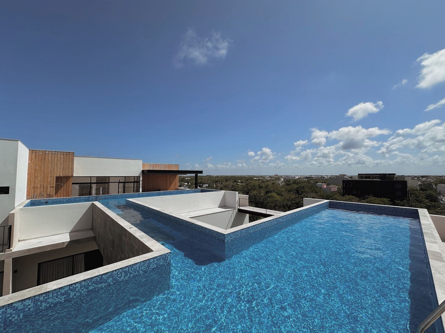 A rooftop swimming pool with clear blue water, surrounded by modern buildings and a clear sky.
