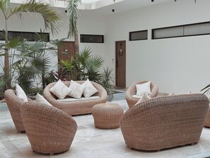A modern interior with wicker furniture, including sofas and ottomans, arranged in a spacious area with a concrete floor and large windows. - Private terrace with jungle views (Tulum)