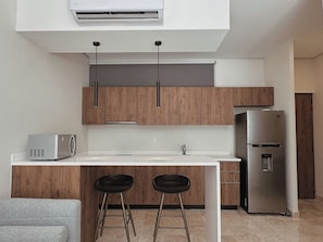 A modern kitchen with wooden cabinets, a stainless steel refrigerator, a microwave, and two bar stools. - Private terrace with jungle views (Tulum)