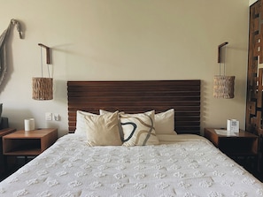 A neatly made bed with a patterned bedspread, two bedside tables with lamps, and a wall-mounted decorative piece. - Please note: electricity is not included in reservations longer than 28... (Tulum)