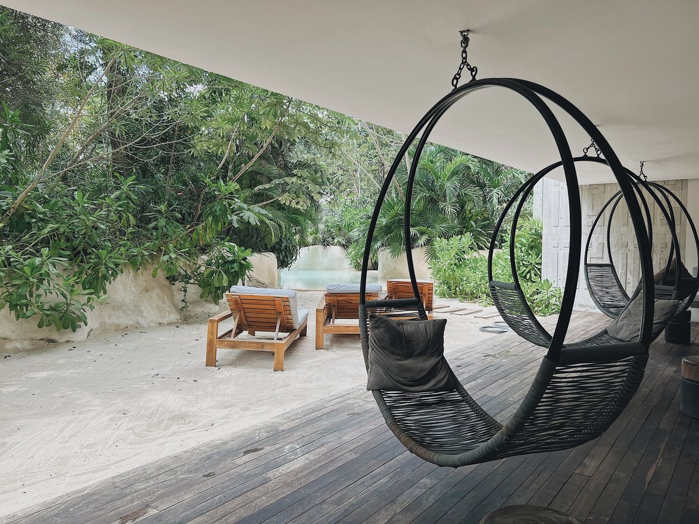 Eine Holzterrasse mit Hängestühlen und einem Tisch, umgeben von üppiger Vegetation.