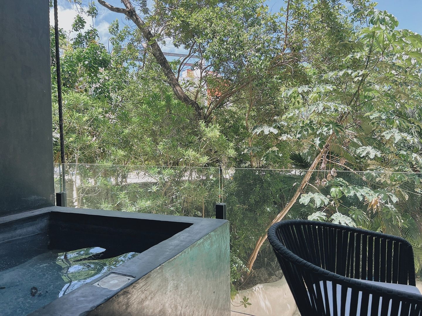 A balcony with a black chair, a concrete planter, and a view of dense foliage.