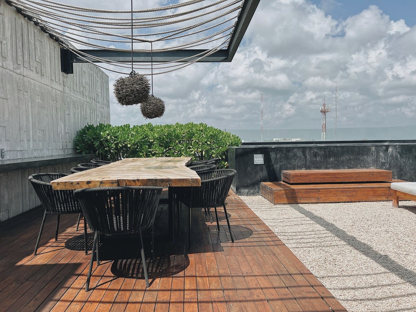 Un espace extérieur aménagé avec une table et des chaises en bois, entouré de verdure et surmonté d’une sorte de tonnelle faite de cordes.