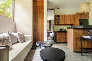 A modern interior with a sofa, a round black table, and a kitchen area with wooden cabinets and a countertop. - Private pool without stairs · 1BR · Selva Tulum (Tulum)