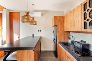 Eine moderne Küche mit Kochinsel, Holzschränken, einem integrierten Kühlschrank und einer schwarzen Arbeitsplatte.