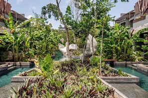 Un espace piscine agrémenté de plusieurs éléments aquatiques, entouré d’une végétation tropicale luxuriante et d’arbres.