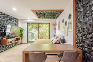 A modern living room with a large wooden dining table, a flat-screen TV, and a sliding glass door leading to a garden. - Caminando a la 5a Ave y la playa (Playa del Carmen)