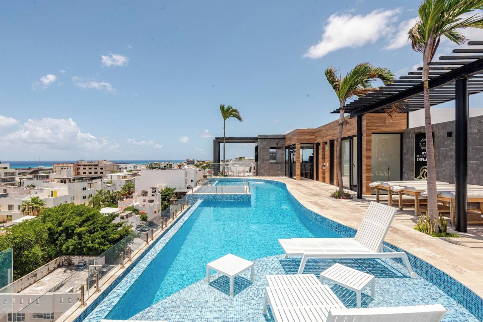 A rooftop infinity pool with lounge chairs, a view of the city, and a spa area.