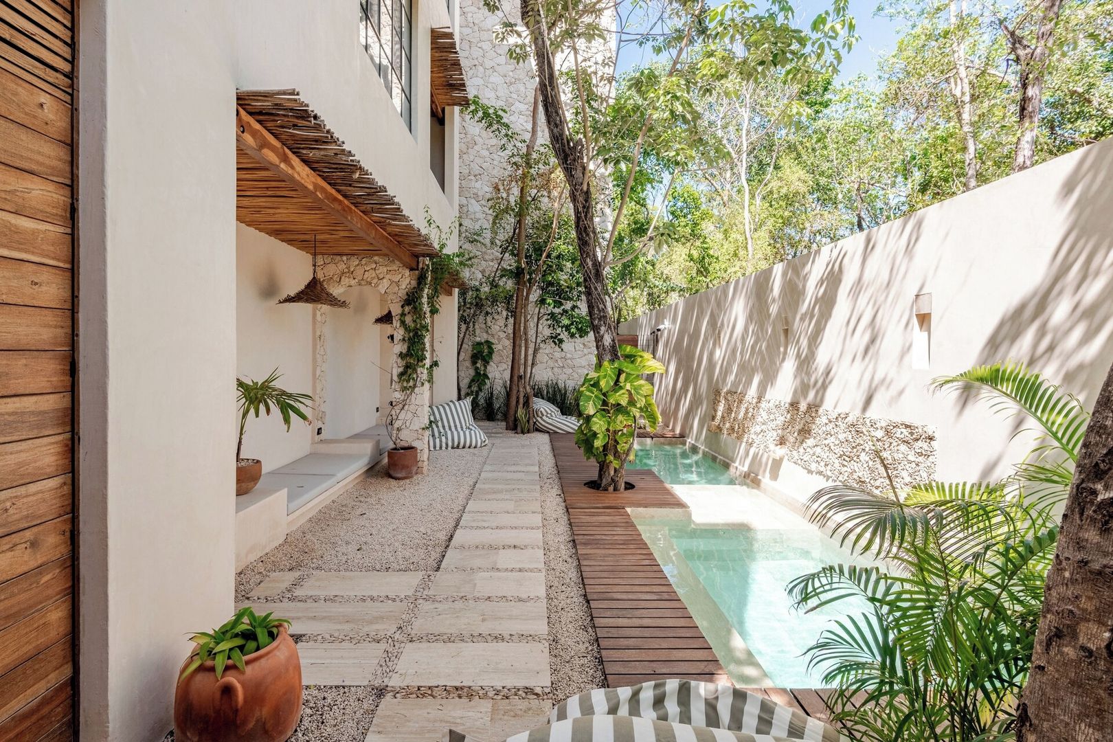 A private pool area with a stone pathway, wooden deck, and potted plants.
