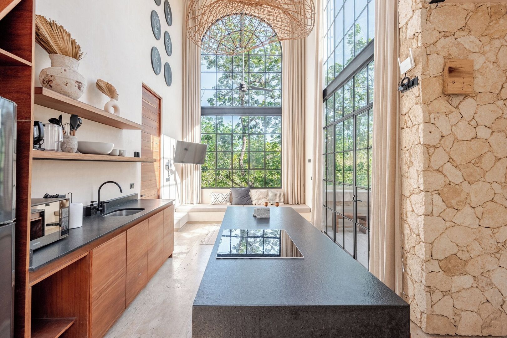 A modern kitchen with a long island counter, wooden cabinets, and a stone accent wall.
