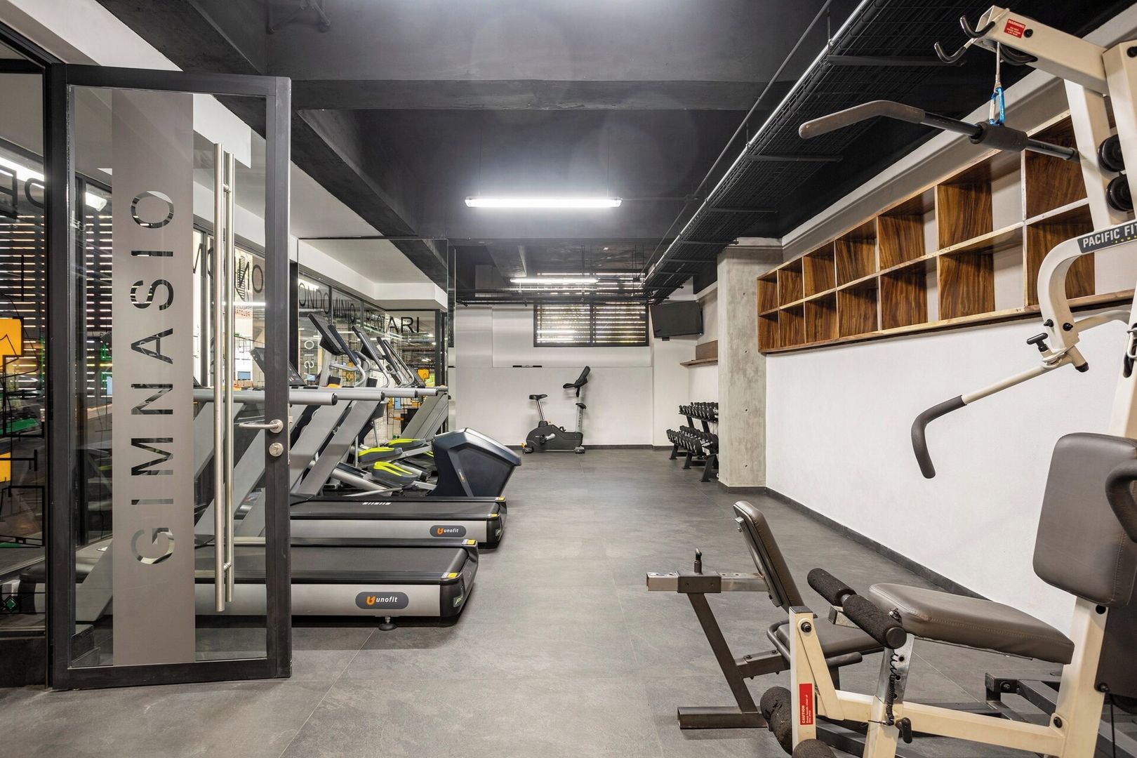 A gym with treadmills, weight machines, and a wall-mounted TV.