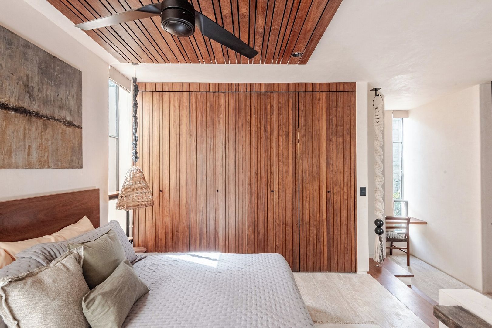 A bedroom with a large bed, a ceiling fan, a wooden wardrobe, and a window.