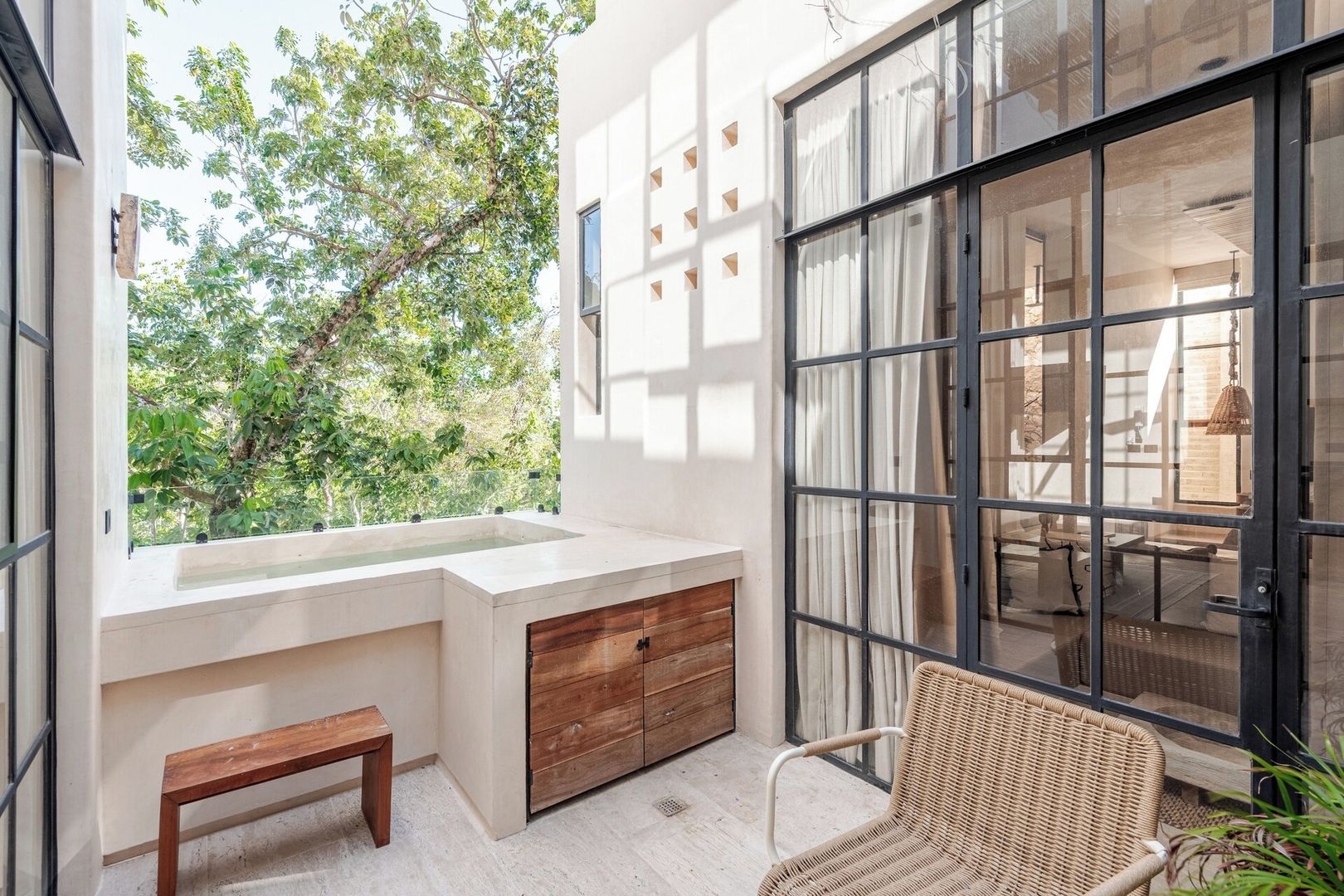 A modern bathroom with a large window, a built-in sink, wooden cabinetry, and a wicker chair.