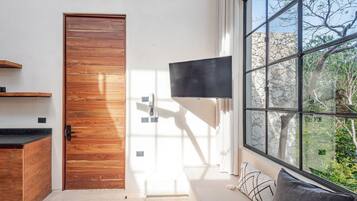 Una camera moderna con una porta in legno, una TV a schermo piatto fissata al muro e un'ampia finestra con vista sugli alberi.