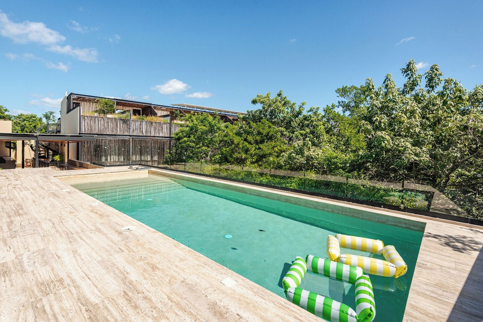 A swimming pool with a wooden deck, surrounded by trees and a wooden fence.