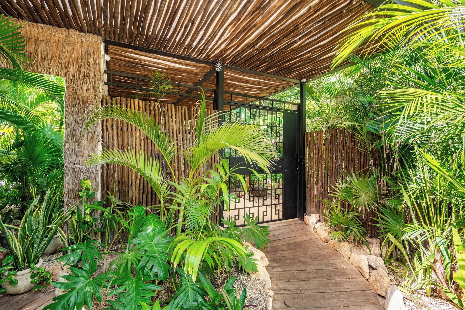 A wooden pathway leading to a gated entrance surrounded by lush tropical plants.