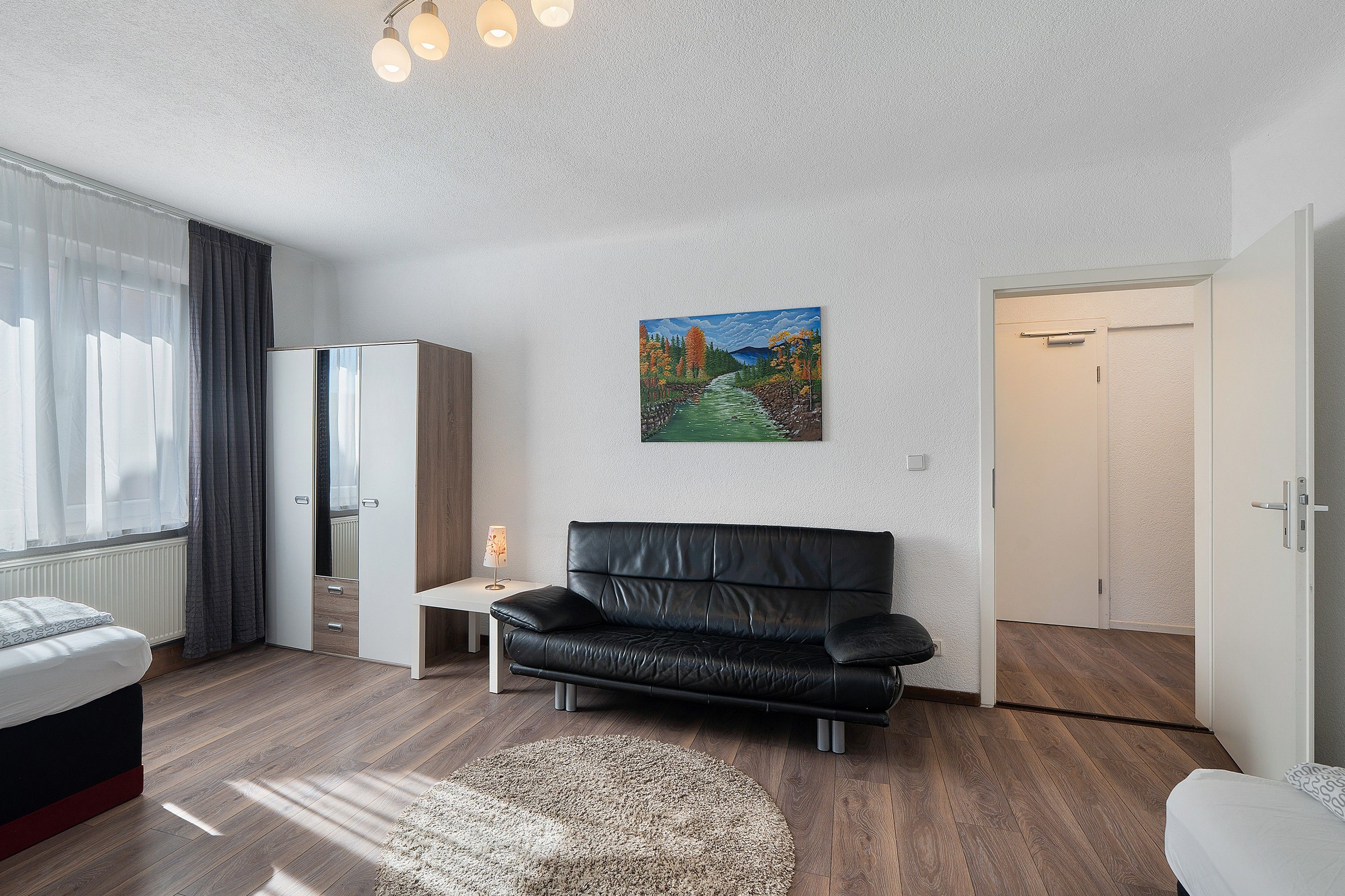 Ein modernes Zimmer mit einer schwarzen Ledersofa, einem kleinen Tisch mit einer Lampe, einem Bild an der Wand und einem Kleiderschrank.