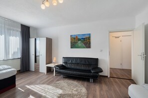 A modern room with a black leather sofa, a small table with a lamp, a painting on the wall, and a wardrobe.