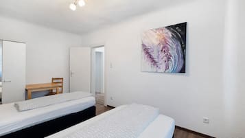 Een hotelkamer met twee bedden, een houten stoel, een schilderij aan de muur en een plafondlamp.