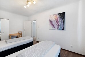 Habitación de hotel con dos camas, una silla de madera, un cuadro en la pared y una lámpara del techo.