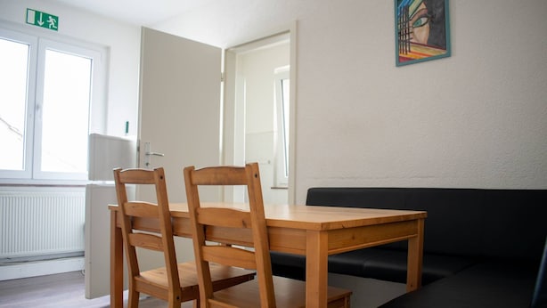 Um quarto com uma mesa e cadeiras de madeira, um sofá preto e um quadro na parede.