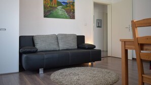 Uma sala de estar moderna com um sofá de couro preto, um tapete redondo bege e uma cadeira de madeira.