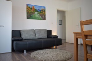 Una sala moderna con un sofá de cuero negro, un tapete redondo color beige y una silla de madera.