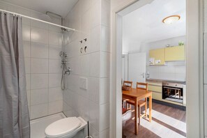Une salle de bain avec douche et toilettes, ainsi qu’un coin repas comprenant une table et des chaises.
