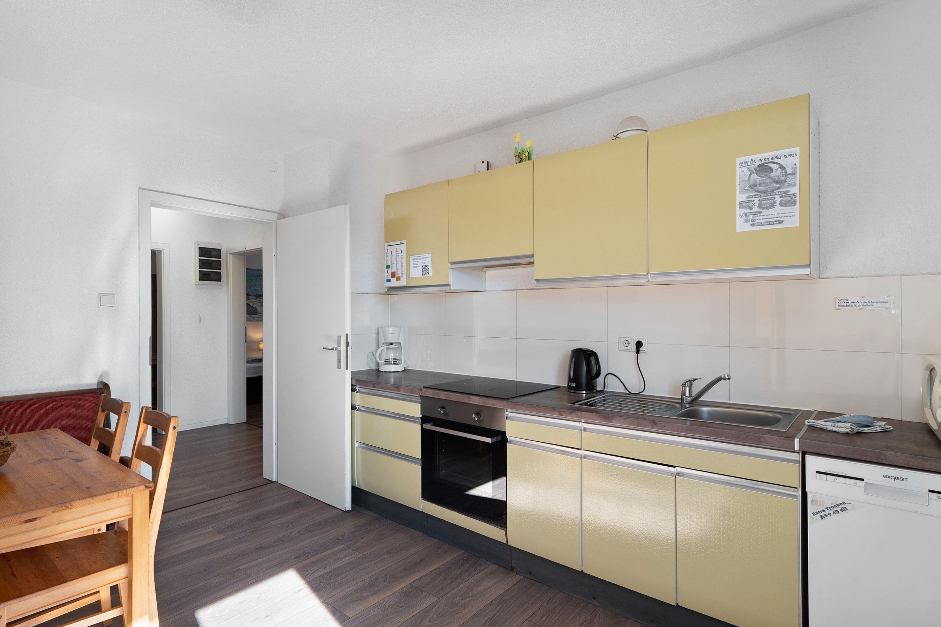 Een kleine keuken met gele kastjes, een ingebouwde oven, een koffiezetapparaat en een vaatwasser.