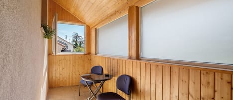 A wooden-paneled room with a table and two chairs, a window, and a view of the outside.