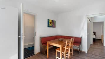 Een kamer met een houten tafel, een bankje, een deur en een kleurrijk abstract schilderij aan de muur.