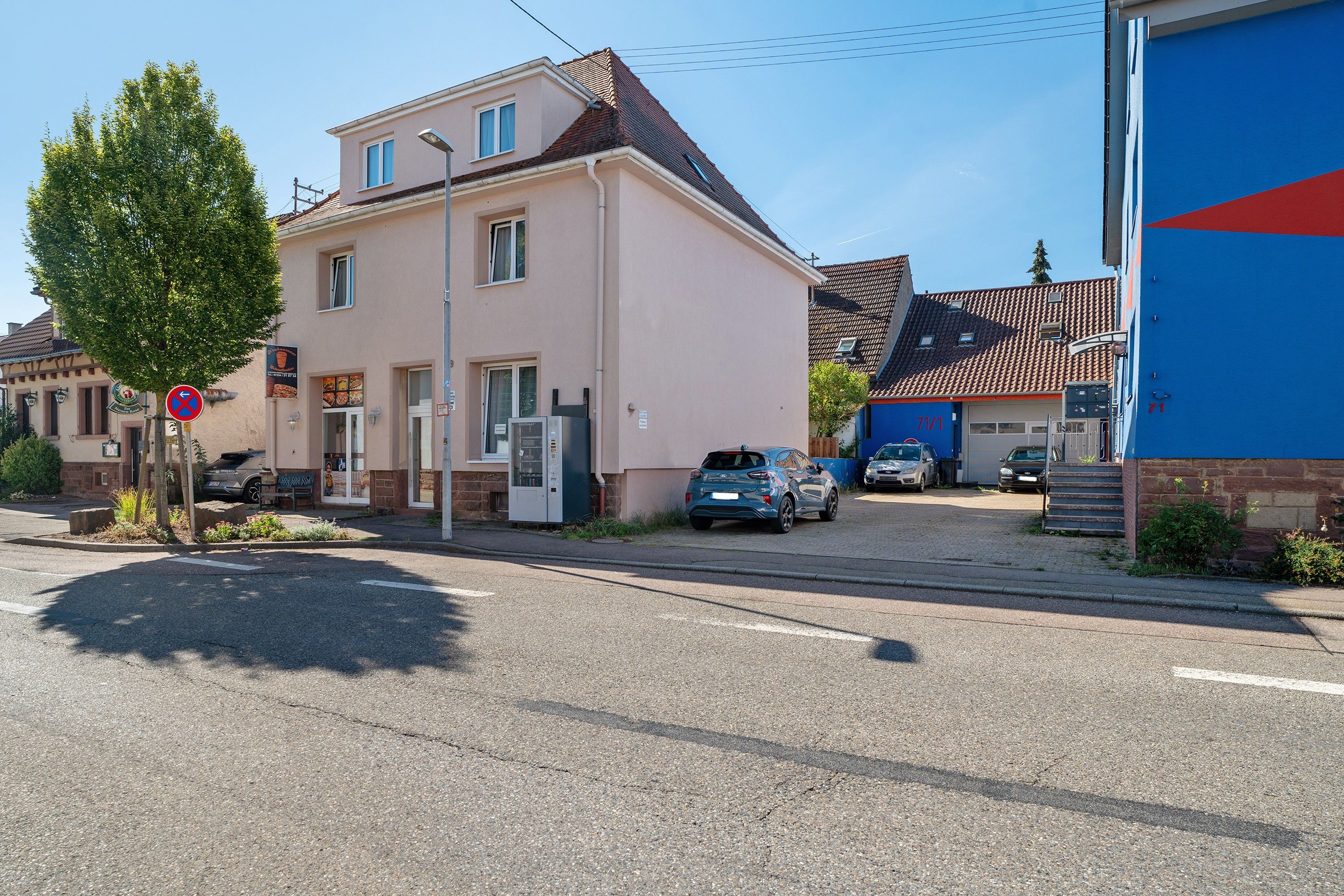Ein zweigeschossiges Gebäude mit flachem Dach, einer sichtbaren Garagentür und einem geparkten Auto davor.