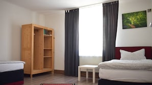 Quarto com cama, guarda-roupa de madeira, mesa pequena e janela com cortinas.
