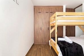 A bunk bed with a wooden frame and a black mattress, a wooden wardrobe with two doors, and a white wall with a light switch. - Romantic design with pool island (Tulum)