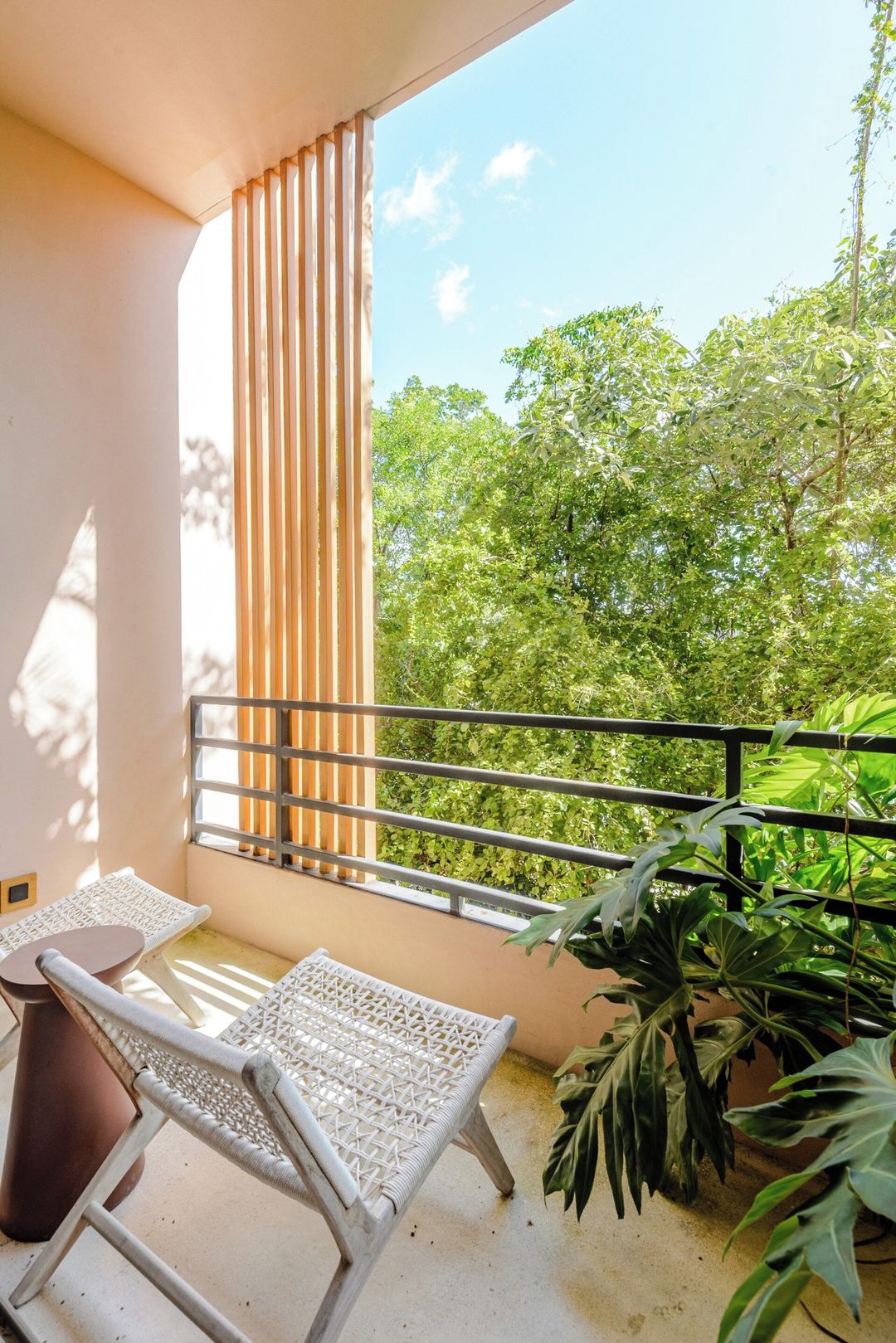 A balcony with a white wicker chair, a small table, and a potted plant.