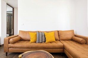 A tan leather sectional sofa with three cushions in a modern living room with a wooden coffee table. - Romantic design with pool island (Tulum)