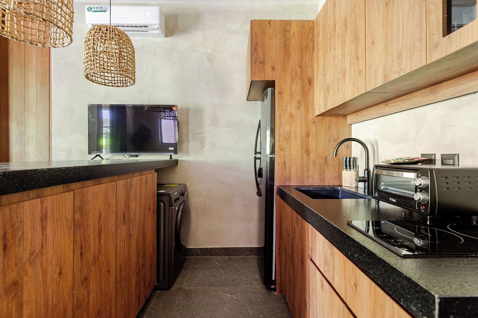 Una cocina compacta con armarios de madera, un microondas integrado, horno tostador y lavadora.