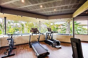 Ein Fitnessstudio mit Laufbändern, Crosstrainern und einem Ergometer, ausgestattet mit großen Fenstern und einer Betondecke.